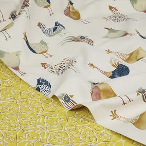 May include: White fabric with a repeating pattern of colorful stylized chickens. The fabric is folded over a yellow fabric with a floral pattern.