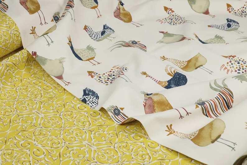 May include: White fabric with a repeating pattern of colorful stylized chickens. The fabric is folded over a yellow fabric with a floral pattern.