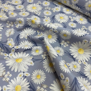May include: A close-up of a light blue fabric with a white daisy pattern. The daisies have yellow centers and are scattered across the fabric.