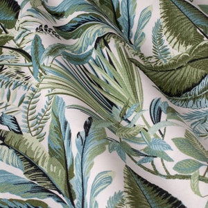 Puede incluir: Tela blanca con un patrón de hojas tropicales en tonos verdes y azules. La tela tiene una textura sutil y un drapeado suave y fluido.