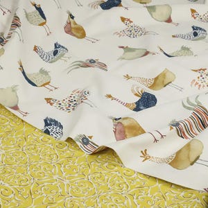 May include: White fabric with a repeating pattern of colorful stylized birds. The fabric is folded and shows a yellow fabric with a floral pattern underneath.