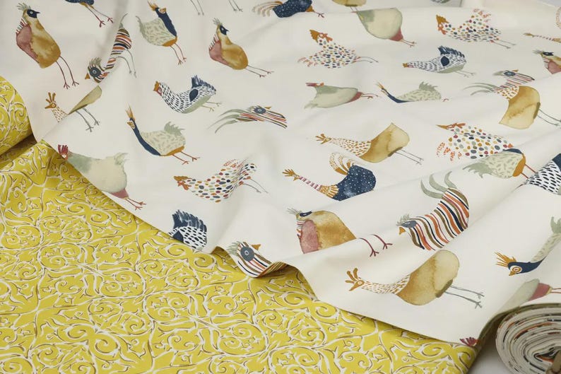 May include: White fabric with a repeating pattern of colorful stylized birds. The fabric is folded and shows a yellow fabric with a floral pattern underneath.