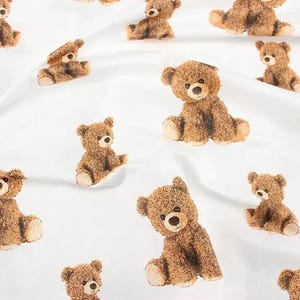 Puede incluir: Tela blanca con un patrón repetido de osos de peluche marrones. Los osos están en varias poses, algunos sentados, algunos de pie y algunos mirando hacia un lado.