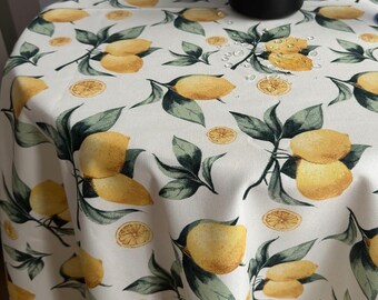 Può includere: Una tovaglia bianca con stampa di limone. La tovaglia ha uno schema di limone giallo con foglie verdi. La tovaglia è su un tavolo rotondo.