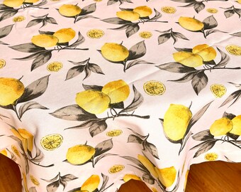 May include: A pink tablecloth with a lemon print. The tablecloth has a white background with yellow lemons and green leaves. The tablecloth is round and has a scalloped edge.