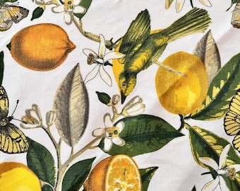 May include: A white fabric with a repeating pattern of lemons, butterflies, birds, and green leaves. The lemons are yellow and some are cut in half to show the inside.
