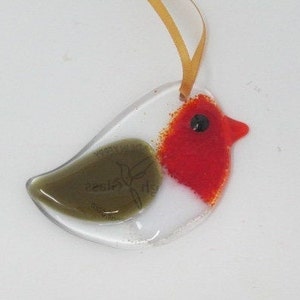 May include: A glass ornament shaped like a robin with a red breast, white belly, and green wings. The ornament has a gold string for hanging.