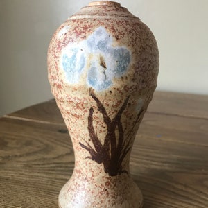 May include: A ceramic vase with a brown and white speckled glaze. The vase has a brown floral design and a white flower design.