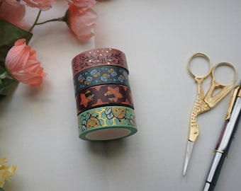 May include: Four rolls of patterned washi tape with gold accents, a pair of gold scissors, and a silver pen on a white notebook.