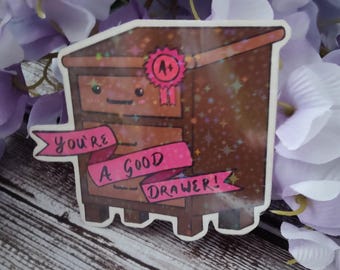 May include: A sticker featuring a cartoon dresser with a pink ribbon that reads "You're a good drawer!" and a pink A+ award. The dresser is brown with a glittery finish and has two drawers. The sticker is surrounded by purple flowers.