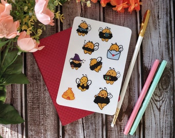 May include: A sheet of stickers featuring cute cartoon bees in various costumes, including a witch, a beekeeper, and a mail carrier. The stickers are on a white background and are perfect for adding a touch of whimsy to your planner, laptop, or water bottle.