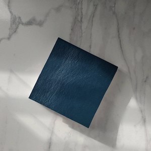 May include: A square piece of dark blue leather with a textured surface.