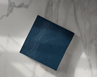 Può includere: Un pezzo quadrato di pelle blu scuro con una superficie testurizzata.
