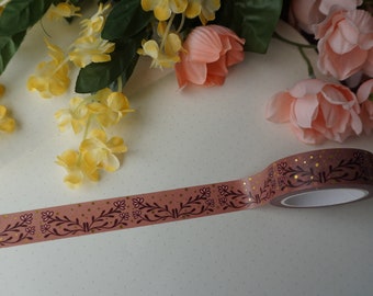 Könnte beinhalten: Eine Rolle Washi-Tape mit rosa Hintergrund und einem burgunderfarbenen Blumenmuster mit goldenen Glitzerakzenten.