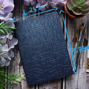 Pu&ograve; includere: Un quaderno blu scuro con un motivo geometrico in rilievo sulla copertina. Il quaderno misura 10,8 cm di larghezza e 14,6 cm di altezza.