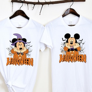 K&ouml;nnte beinhalten: Zwei wei&szlig;e T-Shirts mit Halloween-Motiv. Ein Shirt zeigt Mickey Mouse als Hexe mit dem Text "HALLOWEEN". Das andere Shirt zeigt Mickey Mouse als K&uuml;rbis mit dem Text "HALLOWEEN".