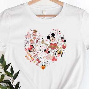 Pode incluir: Camiseta branca com um design em forma de cora&ccedil;&atilde;o com Mickey Mouse, Minnie Mouse, Donald Duck e Pateta. O design inclui cora&ccedil;&otilde;es, estrelas e o texto "Happy Valentine's Day".