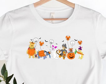 May include: White t-shirt featuring a graphic of Winnie the Pooh and his friends dressed in Halloween costumes. The characters are holding balloons and walking in a line.