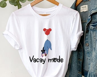 Könnte beinhalten: Weißes T-Shirt mit einem Cartoon-Bild eines blauen Esels, der einen roten Ballon mit einer Mickey-Maus-Kopf hält. Der Text "Vacay mode" ist unter dem Bild gedruckt.