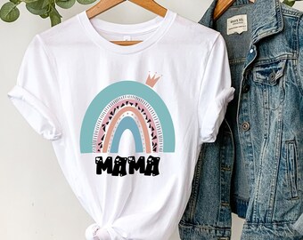 May include: White t-shirt featuring a rainbow design with the word "MAMA" in black lettering. The rainbow has a crown on top and is in shades of pink, orange, and blue.