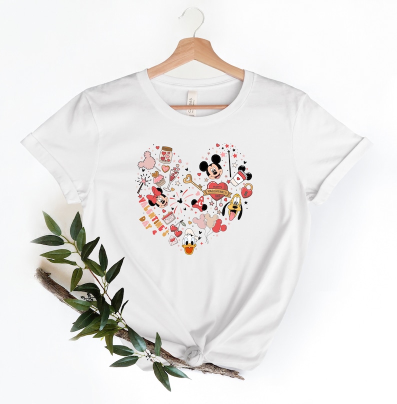 Pode incluir: Camiseta branca com um design em forma de cora&ccedil;&atilde;o com Mickey Mouse, Minnie Mouse, Donald Duck e Pateta. O design inclui cora&ccedil;&otilde;es, estrelas e o texto "Happy Valentine's Day".