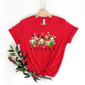 May include: Red t-shirt with a Christmas-themed graphic of Mickey Mouse, Minnie Mouse, Donald Duck, Goofy, and Pluto wearing Santa hats and scarves. The text "FRIENDS" is printed below the characters.