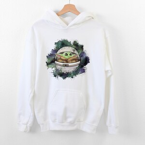 May include: White hooded sweatshirt with a graphic print of a green alien character in a spaceship against a galaxy background.