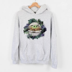 May include: A gray hooded sweatshirt with a graphic print of a green alien character in a spaceship against a galaxy background.