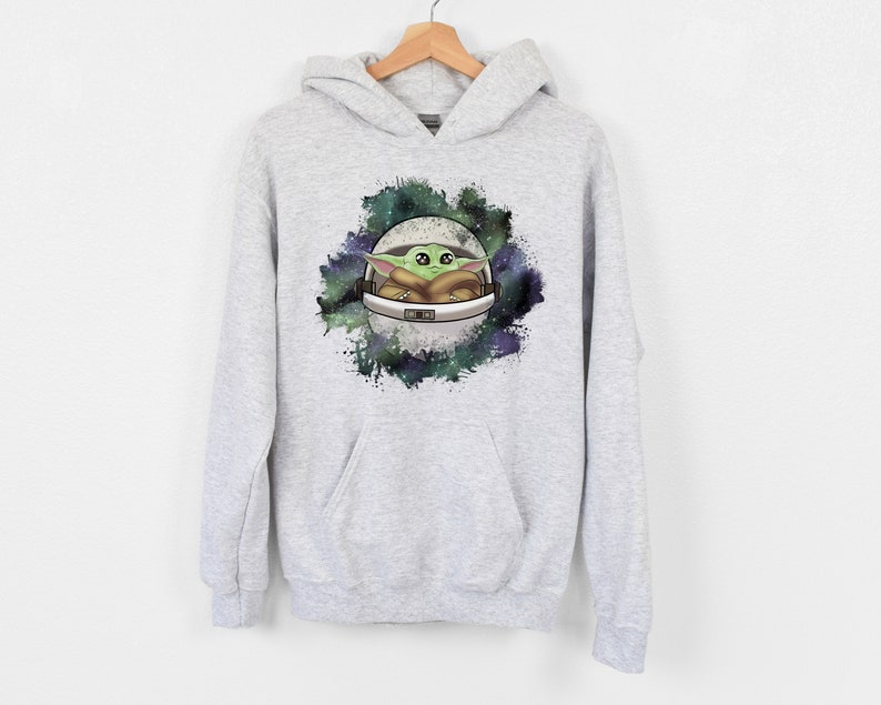 May include: A gray hooded sweatshirt with a graphic print of a green alien character in a spaceship against a galaxy background.