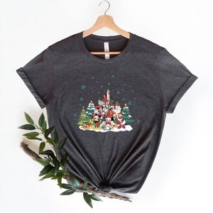 May include: A dark gray t-shirt with a Christmas-themed design featuring Mickey Mouse and other Disney characters in front of a castle. The design includes a snowy scene with Christmas trees and snowflakes.