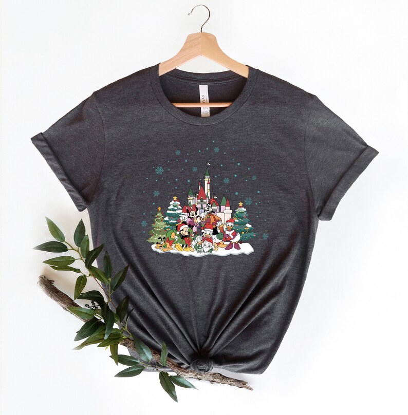 May include: A dark gray t-shirt with a Christmas-themed design featuring Mickey Mouse and other Disney characters in front of a castle. The design includes a snowy scene with Christmas trees and snowflakes.