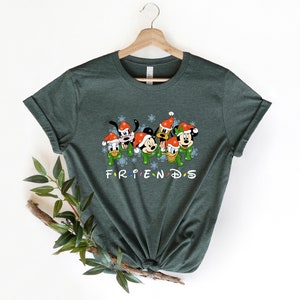 May include: Green t-shirt with a Christmas-themed graphic of Mickey Mouse, Minnie Mouse, Goofy, Donald Duck, and Pluto wearing Santa hats. The text "FRIENDS" is printed below the characters.