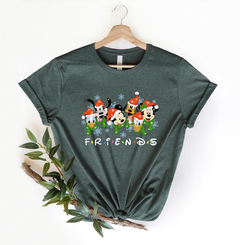 May include: Green t-shirt with a Christmas-themed graphic of Mickey Mouse, Minnie Mouse, Goofy, Donald Duck, and Pluto wearing Santa hats. The text "FRIENDS" is printed below the characters.