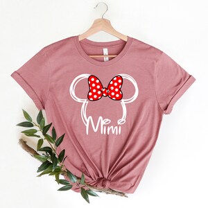 Op de afbeelding: Een mauve t-shirt met een witte omtrek van Mickey Mouse' hoofd met een rode strik met witte stippen. De tekst "Mimi" staat onder het hoofd.