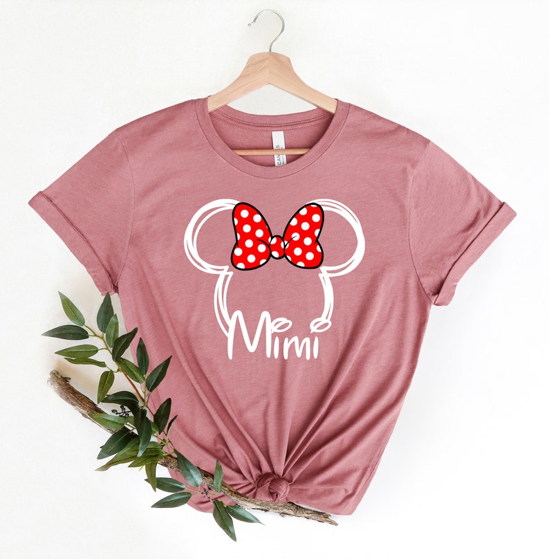 Op de afbeelding: Een mauve t-shirt met een witte omtrek van Mickey Mouse' hoofd met een rode strik met witte stippen. De tekst "Mimi" staat onder het hoofd.