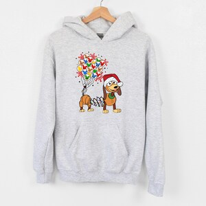 Pu&ograve; includere: Una felpa con cappuccio grigio chiaro con un cane dei cartoni animati con un cappello da Babbo Natale e palloncini. I palloncini presentano disegni di Topolino e fiocchi di neve. Il cane ha un corpo a molla ed &egrave; un design festivo per le vacanze.