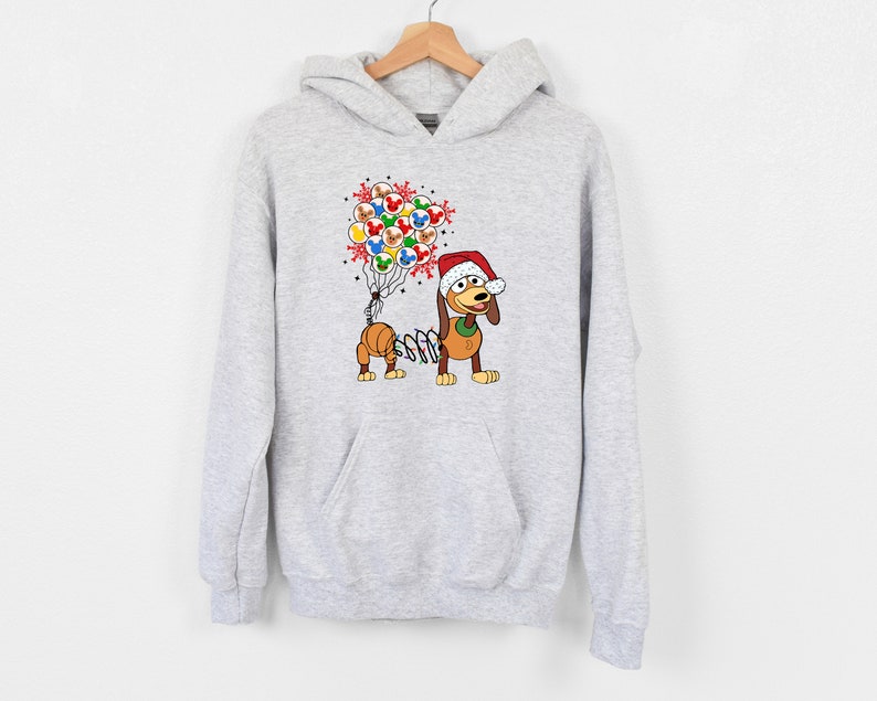 Pu&ograve; includere: Una felpa con cappuccio grigio chiaro con un cane dei cartoni animati con un cappello da Babbo Natale e palloncini. I palloncini presentano disegni di Topolino e fiocchi di neve. Il cane ha un corpo a molla ed &egrave; un design festivo per le vacanze.