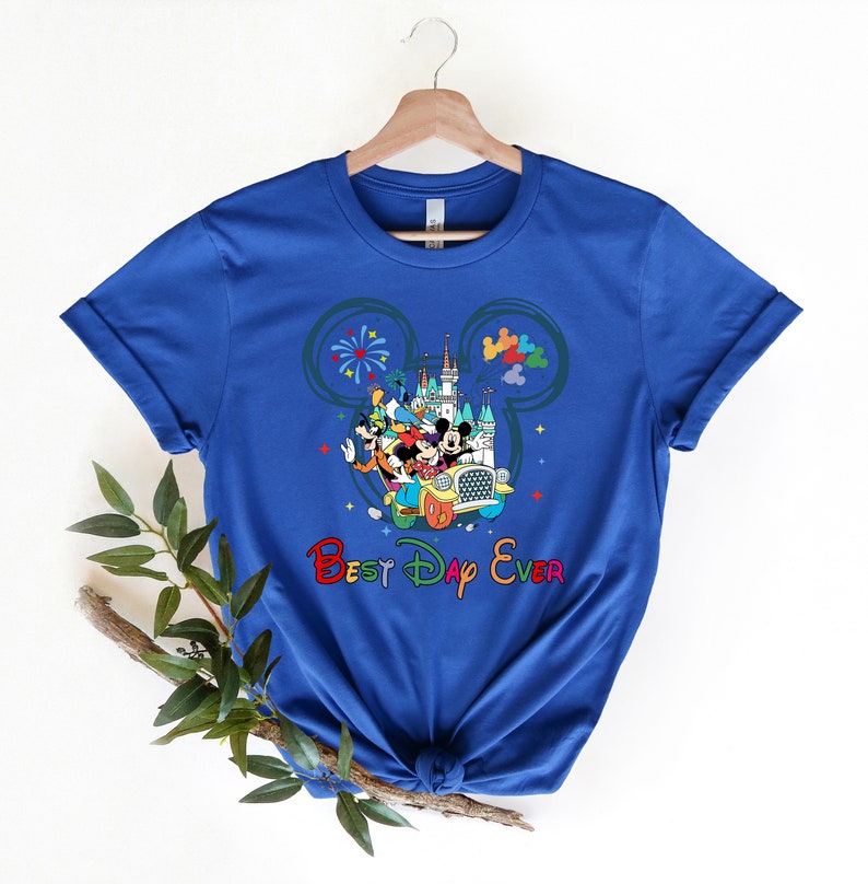 May include: A royal blue t-shirt with a colorful graphic of Mickey Mouse and friends in a car in front of the Cinderella Castle. The graphic is inside a Mickey Mouse ear outline. The text "Best Day Ever" is below the graphic in rainbow colors.