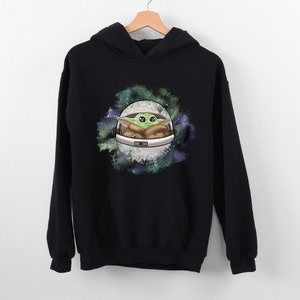 May include: Black hooded sweatshirt with a graphic print of a green alien character in a spaceship against a galaxy background.