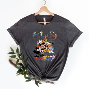 Puede incluir: Una camiseta gris oscuro con un gr&aacute;fico colorido de Mickey Mouse, Minnie Mouse, Donald Duck, Goofy y Pluto frente al Castillo de Cenicienta. El gr&aacute;fico tambi&eacute;n incluye el texto "Disney Family Vacation" y el a&ntilde;o "2024".