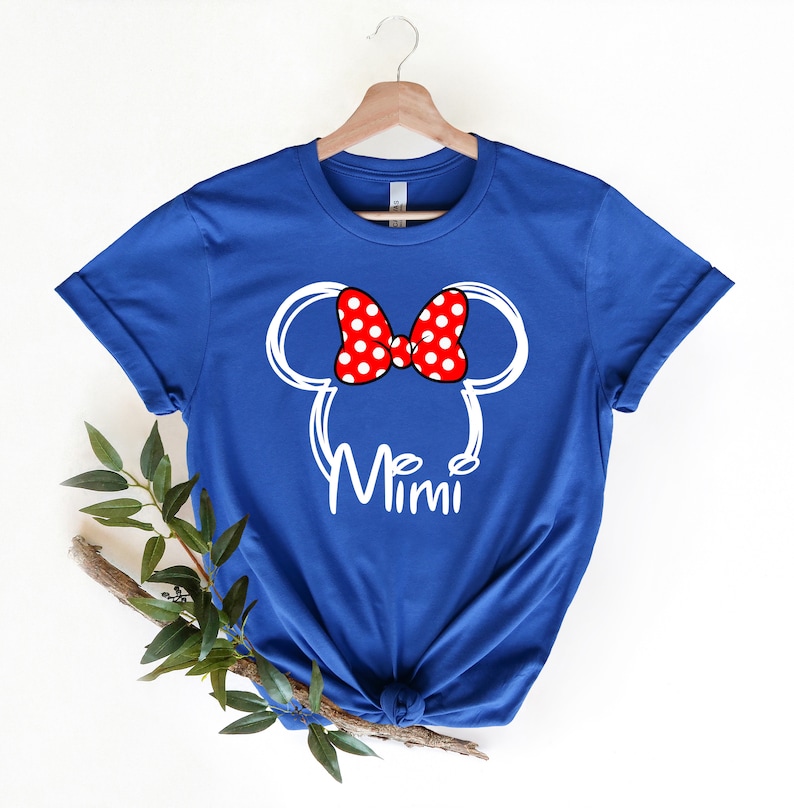 Op de afbeelding: Blauw T-shirt met een witte omtrek van Mickey Mouse oren en een rode strik met witte stippen. De tekst "Mimi" is onder de oren gedrukt.