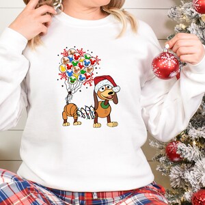Pu&ograve; includere: Felpa bianca con un cane dei cartoni animati con un cappello da Babbo Natale e una stringa di luci. Il cane &egrave; accompagnato da un gruppo di palloncini a tema Mickey Mouse. Il design &egrave; festivo e a tema vacanze.