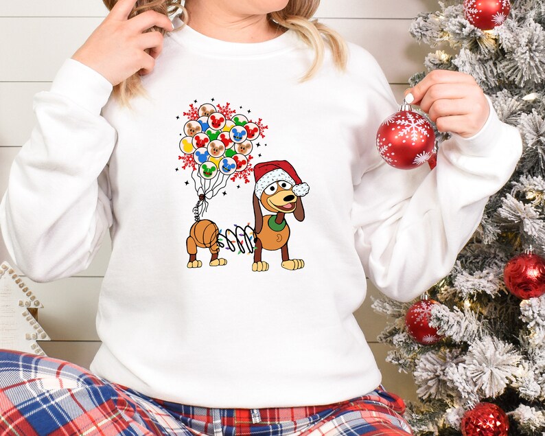 Pu&ograve; includere: Felpa bianca con un cane dei cartoni animati con un cappello da Babbo Natale e una stringa di luci. Il cane &egrave; accompagnato da un gruppo di palloncini a tema Mickey Mouse. Il design &egrave; festivo e a tema vacanze.