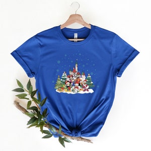 May include: A royal blue t-shirt with a Christmas-themed design featuring Mickey Mouse and friends in front of a castle. The design includes snow, Christmas trees, and snowflakes.