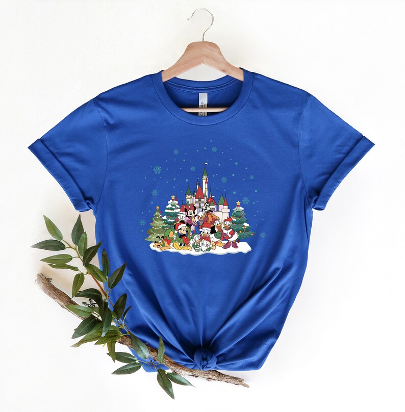 May include: A royal blue t-shirt with a Christmas-themed design featuring Mickey Mouse and friends in front of a castle. The design includes snow, Christmas trees, and snowflakes.