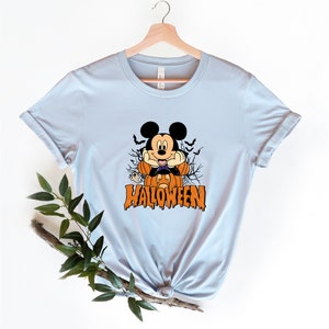 K&ouml;nnte beinhalten: Hellblaues T-Shirt mit einem Aufdruck von Mickey Mouse als Vampir, der einen K&uuml;rbis h&auml;lt. Der Text "HALLOWEEN" ist unter Mickey Mouse gedruckt.