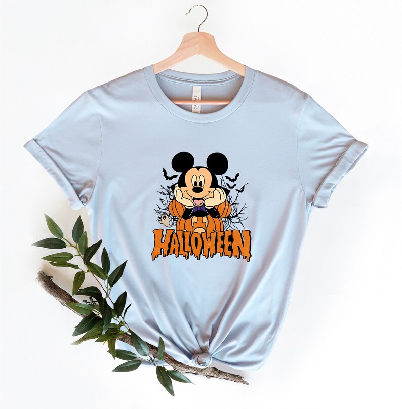 K&ouml;nnte beinhalten: Hellblaues T-Shirt mit einem Aufdruck von Mickey Mouse als Vampir, der einen K&uuml;rbis h&auml;lt. Der Text "HALLOWEEN" ist unter Mickey Mouse gedruckt.