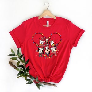 May include: Red t-shirt with a Christmas-themed design featuring Mickey Mouse, Minnie Mouse, Donald Duck, Goofy, and Pluto wearing Santa hats and scarves. The design is in the shape of Mickey Mouse's head with Christmas lights around it.