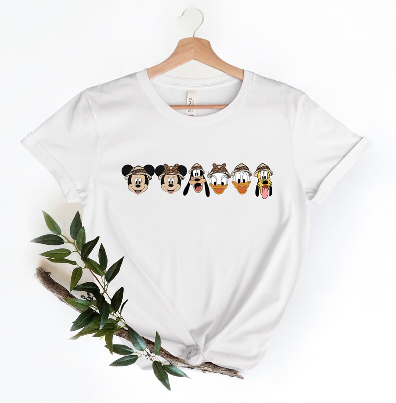 May include: White t-shirt with a line of five cartoon characters wearing safari hats. The characters are Mickey Mouse, Minnie Mouse, Goofy, Donald Duck, and Pluto.