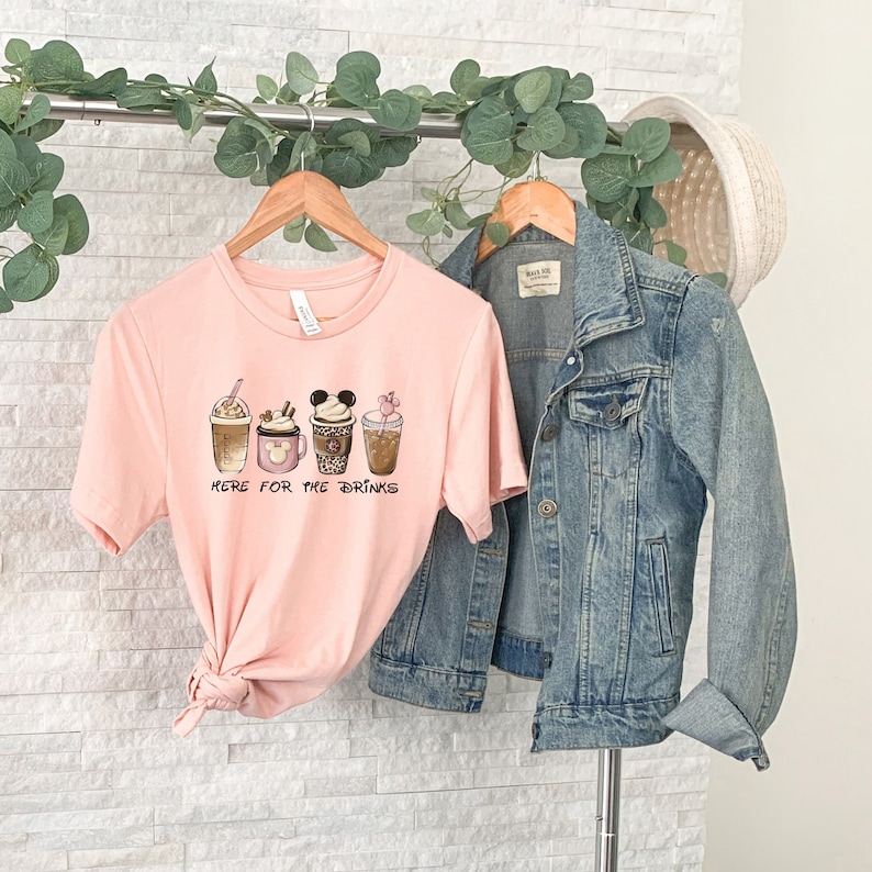 May include: A pink t-shirt with a graphic of five different coffee drinks. The text "Here for the drinks" is printed below the graphic.
